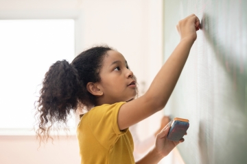 Female student writing on school classroom chalkboard