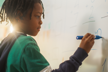 Student doing math on a white board in classroom