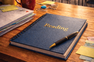 Notebook labeled ‘Reading’ with a pen on a desk, representing early literacy instruction and reading education.