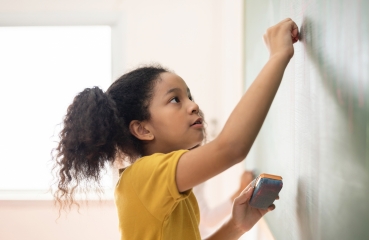 Female student writing on school classroom chalkboard