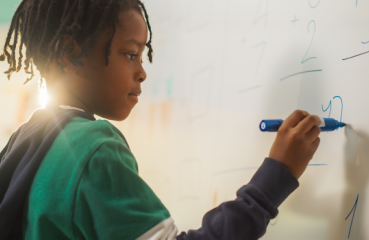 Student doing math on a white board in classroom