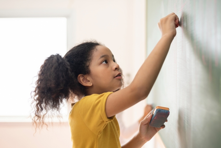Female student writing on school classroom chalkboard