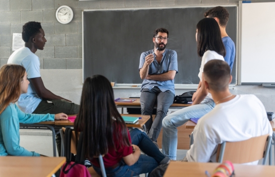 Young teacher talking with teenager students seating in a circle at school